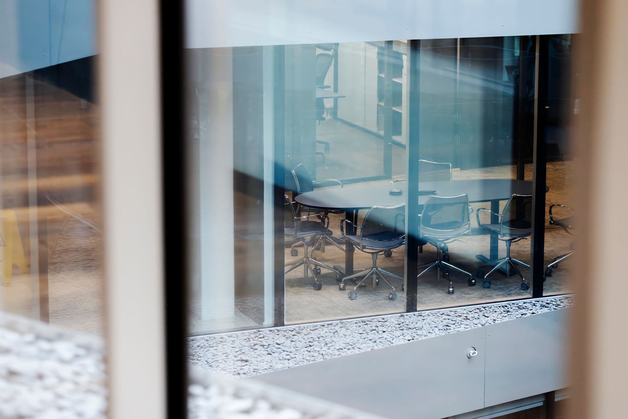 A glass-walled meeting room seen from outside, chairs gathered around an empty table