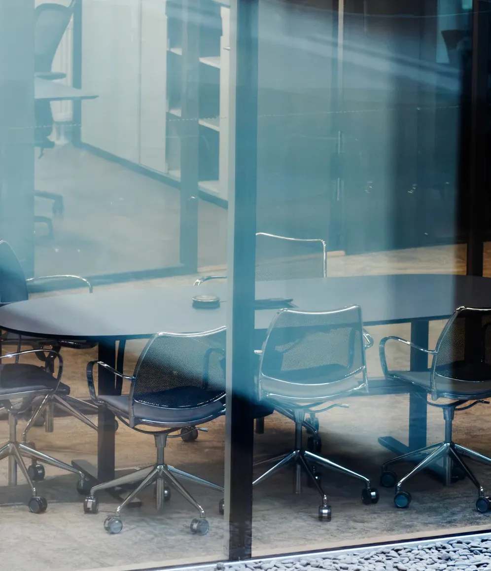 A glass-walled meeting room seen from outside, chairs gathered around an empty table